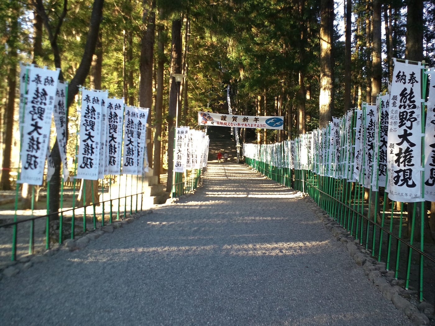 Stone lanterns and approach to Kumano Hongu Taisha shrine in Wakayama, Japan, where the three-legged crow Yatagarasu is enshrined, with the shrine's Yatagarasu emblem visible on signage.